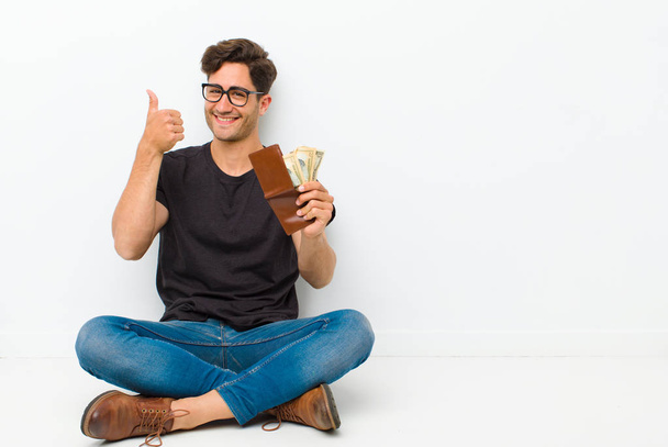 young handsome man with a wallet sitting on the floor sitting on the floor in a white room - Foto, afbeelding