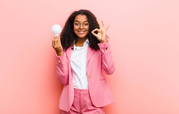 young black pretty woman with a light bulb having an idea against pink wall background - Foto, imagen