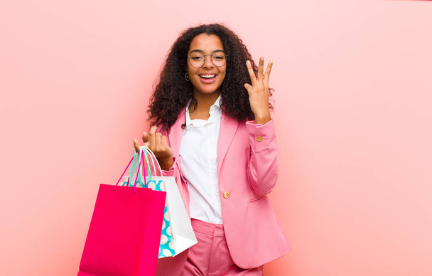 young black pretty woman with shopping bags against pink wall background - 写真・画像