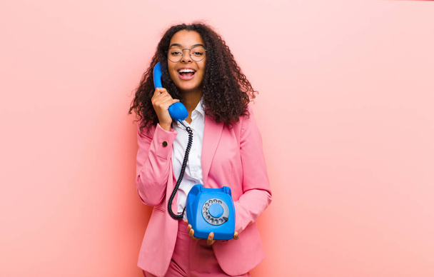 fiatal fekete csinos nő egy vintage telefon ellen rózsaszín fal háttér - Fotó, kép
