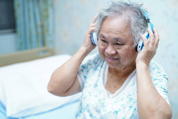 Asiática senior o anciana anciana mujer paciente escuchar música mientras se acuesta en la cama en enfermería hospital sala: saludable fuerte concepto médico
 - Foto, Imagen