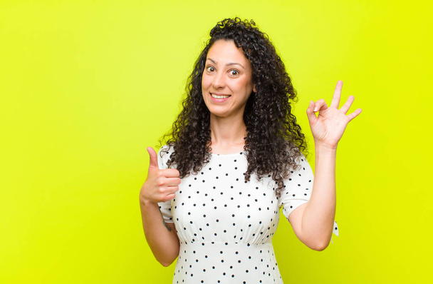 young pretty woman feeling happy, amazed, satisfied and surprised, showing okay and thumbs up gestures, smiling against chroma key wall - Foto, immagini