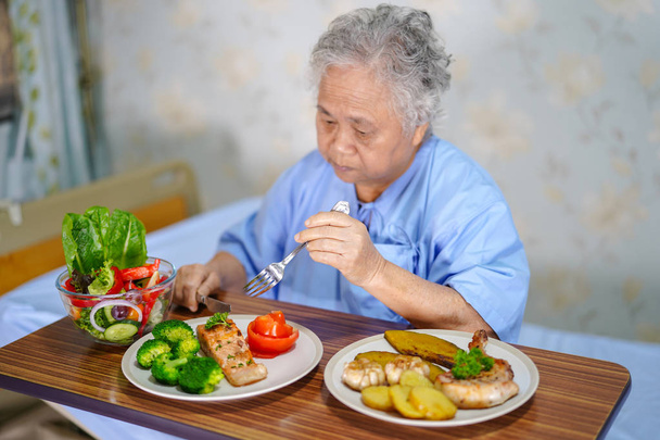 Aziatische senior of ouderen oude dame vrouw patiënt gezond eten van de ontbijt met hoop en gelukkig zittend en hongerig op bed in het ziekenhuis - Foto, afbeelding