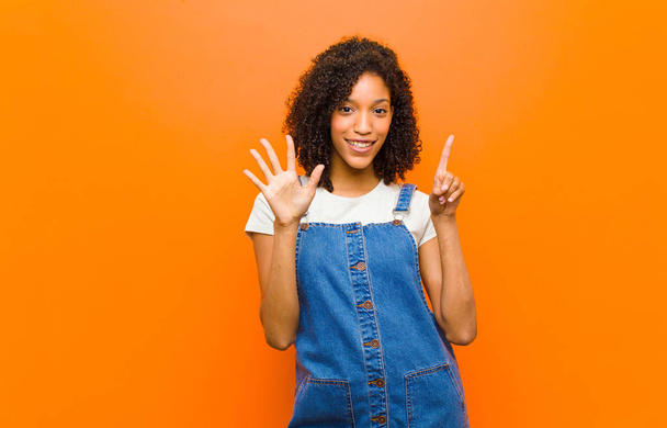 young pretty black woman smiling and looking friendly, showing number six or sixth with hand forward, counting down against orange wall - Foto, immagini