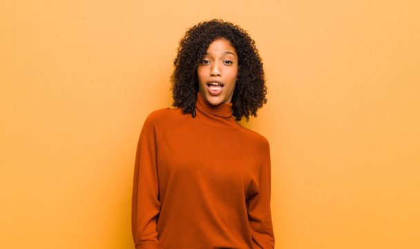 young pretty black woman with a big, friendly, carefree smile, looking positive, relaxed and happy, chilling against orange wall - Zdjęcie, obraz
