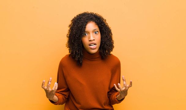 młoda ładna czarna kobieta patrząc zły, zdenerwowany i sfrustrowany krzyczy wtf lub co jest z tobą nie tak pod pomarańczową ścianą  - Zdjęcie, obraz