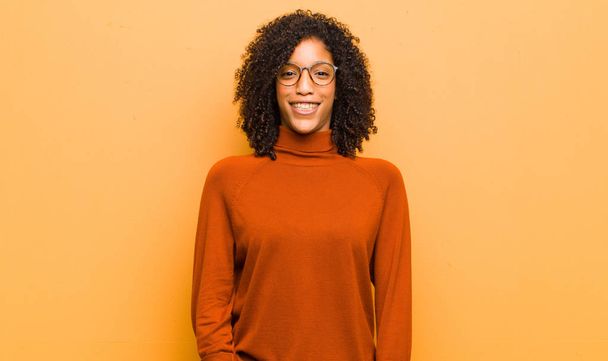 young pretty black woman looking happy and pleasantly surprised, excited with a fascinated and shocked expression against orange wall - Фото, зображення