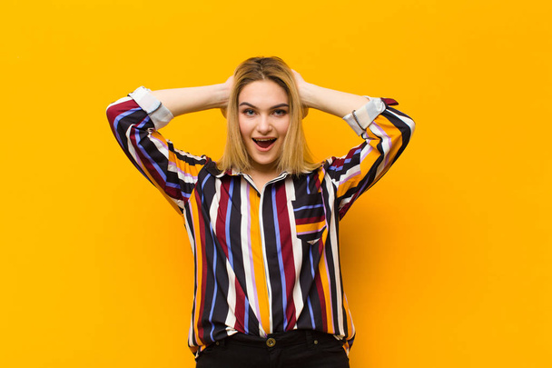 young blonde pretty woman looking happy, carefree, friendly and relaxed enjoying life and success, with a positive attitude against orange wall - Foto, Imagem