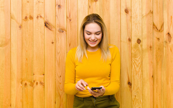 young pretty blonde woman with a mobile phone against wood wall - Foto, imagen