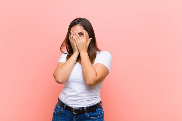 young pretty hispanic woman feeling stressed, worried, anxious or scared, with hands on head, panicking at mistake against pink wall - Фото, изображение