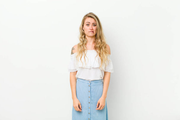 young blonde woman feeling clueless, confused and uncertain about which option to pick, trying to solve the problem against white wall - Fotoğraf, Görsel