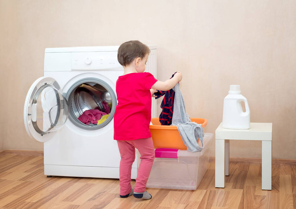 Little girl holding clothes near a washing machine - Fotó, kép