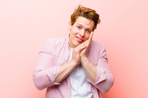 young red head man feeling in love and looking cute, adorable and happy, smiling romantically with hands next to face against pink wall - Photo, Image