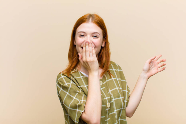 young red head pretty woman feeling happy, shocked and surprised, covering mouth with hand and pointing to lateral copy space - Photo, image