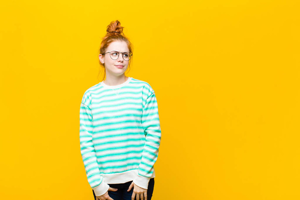 young red head woman wondering, thinking happy thoughts and ideas, daydreaming, looking to copy space on side against orange wall - Fotoğraf, Görsel