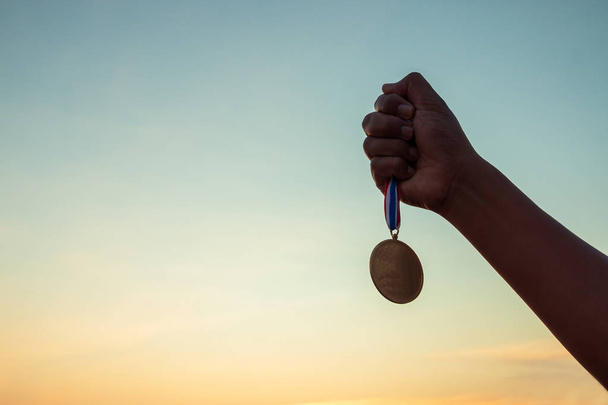 Концепції перемоги, успіху, Руки з нагородою, яка завоювала медаль на прекрасному заході сонця. - Фото, зображення