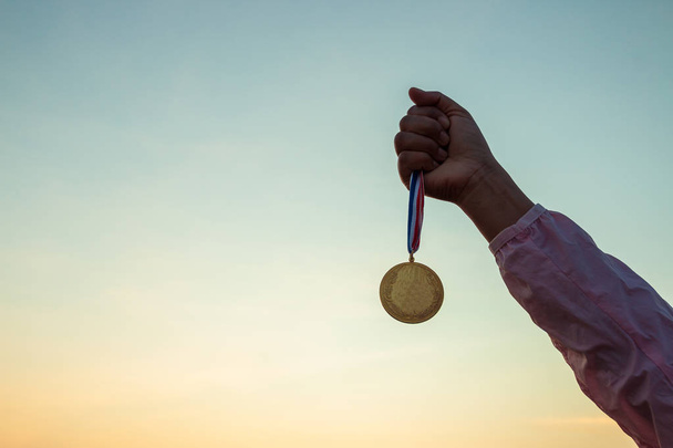 Concepten van overwinning, succes, vrouw draagt roze shirts met lange mouwen. Houdt gouden medaille op prachtige zonsondergang hemel achtergrond. - Foto, afbeelding