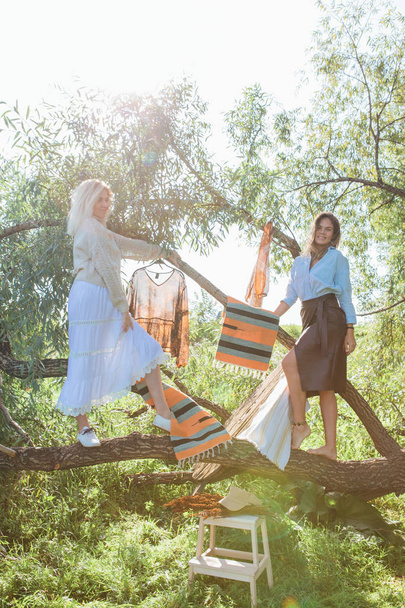 Portrait of two beautiful women brunette and blond standing on the big brunch of tree in a field in late summer. Beautiful girls standing next to each other. - Φωτογραφία, εικόνα
