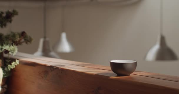 Male hand putting black and white teacups on wooden desk indoors natural sunny light 4k. Faceless teamaster demonstrating teaware for tea ceremony inside sunny apartment slow motion close up - Footage, Video