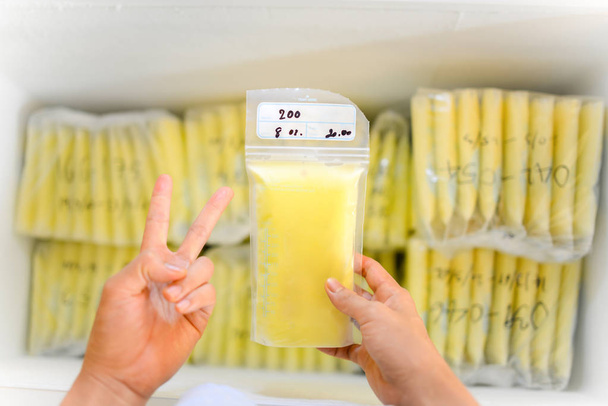 Mains tenant le sac de stockage de lait maternel devant les stocks dans le réfrigérateur congélateur
 - Photo, image