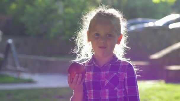 enfant mord pomme dans le contre-jour, petite fille habillée chemise mâche fruits mûrs juteux et regarder la caméra à la nature
 - Séquence, vidéo
