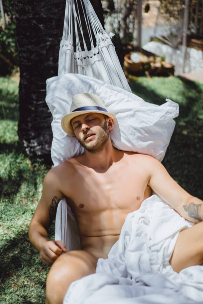 nude male relaxing in a hammock in the garden. - Zdjęcie, obraz