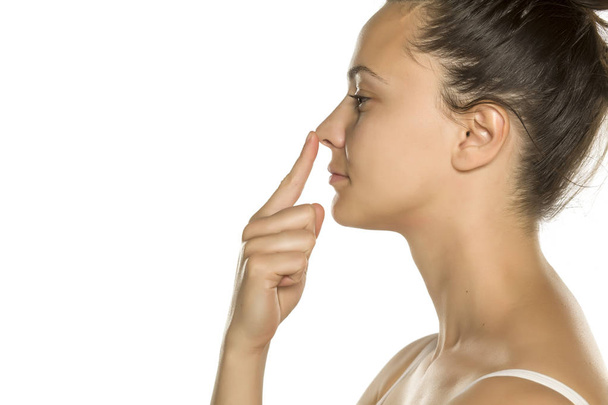 young woman touches her nose with her finger on a white background - Fotoğraf, Görsel