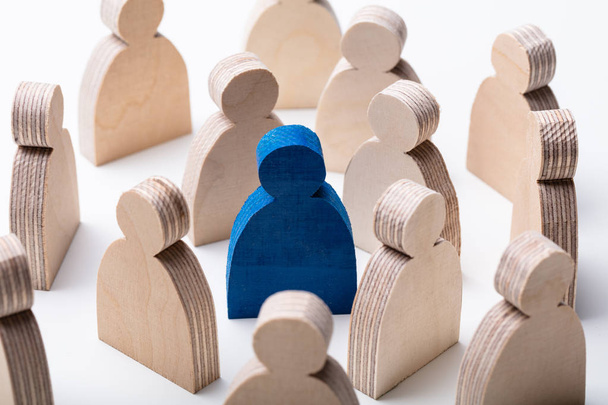 Close-up Of A Blue Human Figure Surrounded With Wooden Figures Over White Desk - Foto, Imagen