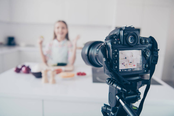Close-up view of professional cam recording video lesson attractive beautiful cheerful cheery pre-teen girl making useful vitamin vegs salad dish in light white interior kitchen house indoors - Photo, Image