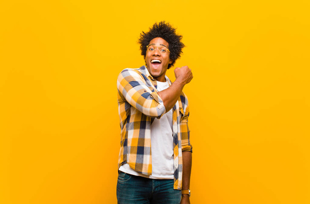 young black man feeling happy, positive and successful, motivated when facing a challenge or celebrating good results against orange wall - Fotoğraf, Görsel
