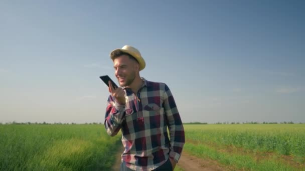 happy emotions while talking on mobile phone, farmer in straw hat and checkered shirt walking along a country road in his field - Materiał filmowy, wideo