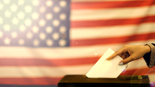 femme qui met un bulletin de vote dans une urne le jour du scrutin. Gros plan de la main avec papier de votes blancs sur fond de drapeau des Etats-Unis
. - Photo, image