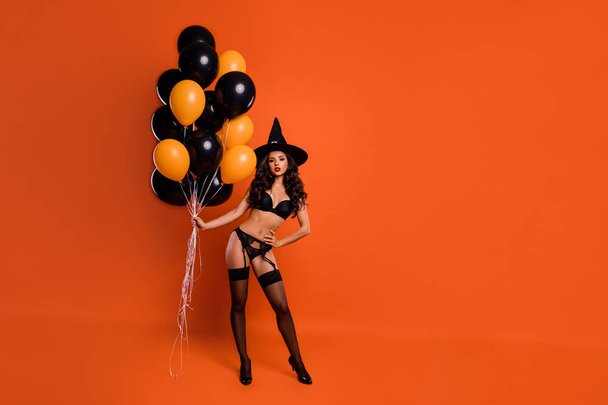 Full length photo of beautiful red lips nude lady hold air balloons demonstrate perfect shapes naughty mood wear bikini tights witch cap isolated orange background - Foto, Bild