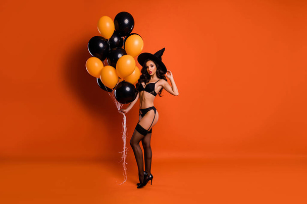 Full length photo of beautiful nude lady hold air balloons make private party showing husband ideal figure wear black bikini tights witch cap isolated orange background - Fotó, kép