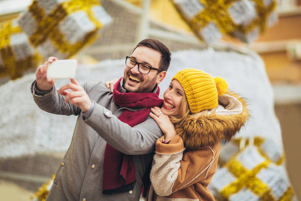 Young beautiful couple with Santa hats make selfie photo in the city. - Фото, зображення