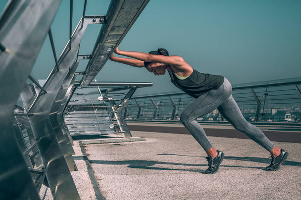 Professional sportswoman training on the bridge and stretching her body by the banister - Foto, immagini