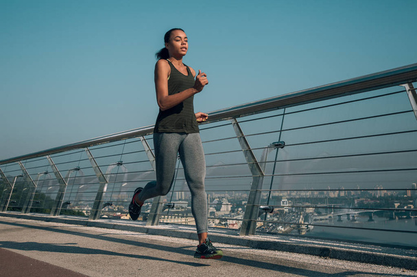Relaxed young sportswoman looking calm while jogging on the bridge - Foto, Imagen