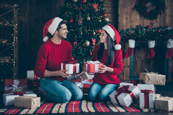 Full size profile side photo of two romantic married people in cap hat give packages on christmas time sit on plaid blanket in house with newyear decoration indoors - Fotoğraf, Görsel