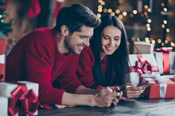 Close up photo of two romantic people lying on floor with gift boxes using device looking blogs enjoy noel x-mas holidays christmas party in house full of newyear lights indoors - Zdjęcie, obraz