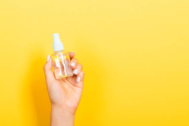 Female hand holding spray cream bottle of lotion isolated. Girl give cosmetic products on yellow background - Φωτογραφία, εικόνα