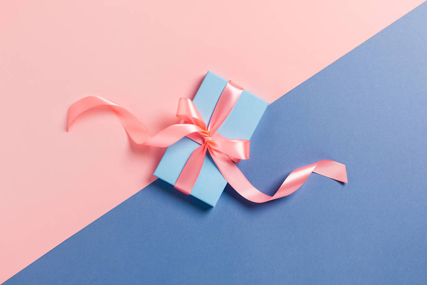 Biglietto natalizio. Una scatola blu con un fiocco rosa su sfondo bicolore. - Foto, immagini