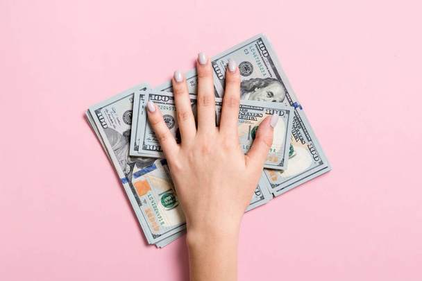 Female hand lying on stack of one hundred dollar bills on colorful background. Saving money and wellbeing concept - Photo, Image