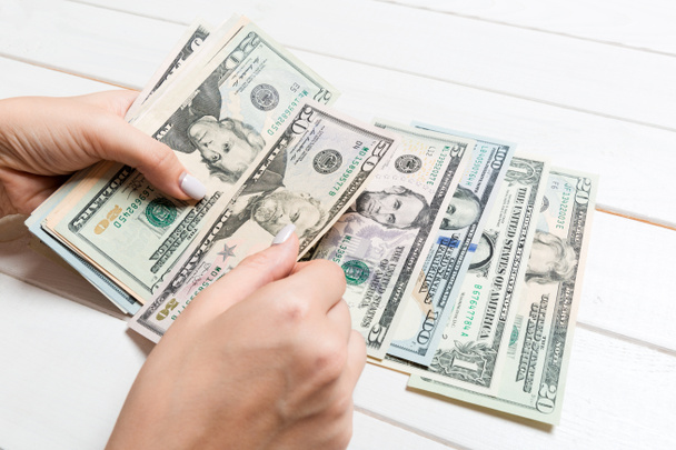 Perspectief beeld van vrouwelijke handen die geld tellen. Verschillende dollarbiljetten op houten ondergrond. Bedrijfsconcept - Foto, afbeelding