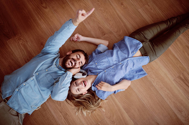 Top view of attractive caucasian couple lying on the floor, listening music over the headphones and singing. - Photo, Image