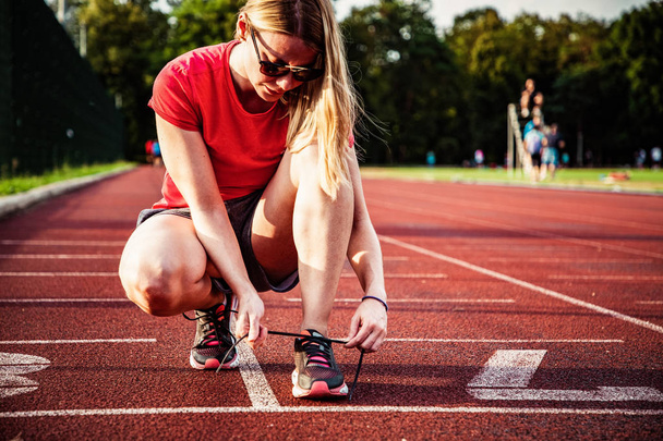 young woman on running track lacing shoes - Foto, Imagem