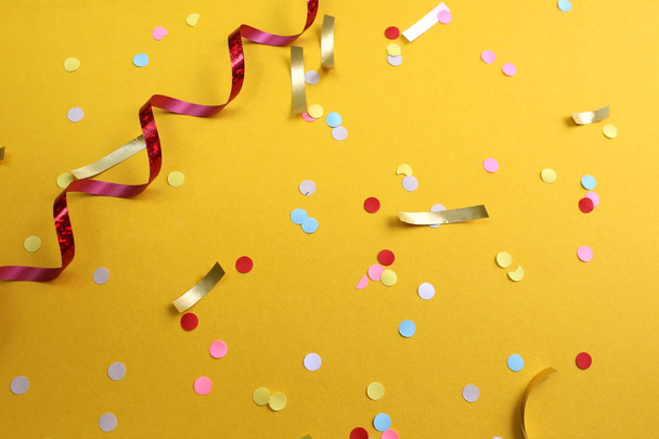 on a yellow background lies a swirling ribbon and festive confetti - Foto, imagen