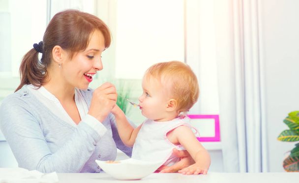 Mother feeding her baby girl with a spoon. Baby food. Healthy family - Zdjęcie, obraz