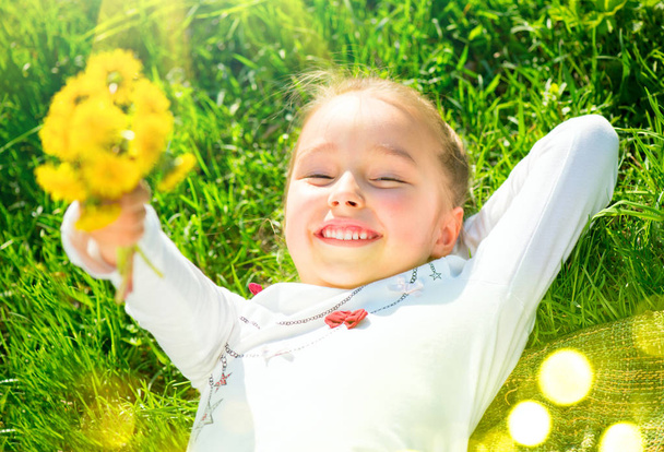 Porträt eines lächelnden kleinen Mädchens, das mit einem Bu auf grünem Gras liegt - Foto, Bild