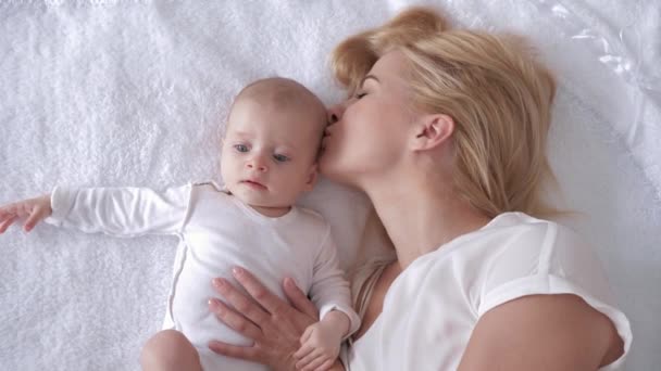 beste momenten uit het leven, liefdevolle gelukkige jonge moeder knuffels en kusjes een pasgeboren dochter op deken en kijk op camera - Video