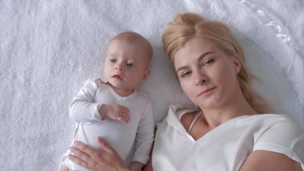 Rodina a štěstí, milující mladá matka objetí a polibky novorozené dcery ležící na bílém pozadí a pohled na kameru - Záběry, video